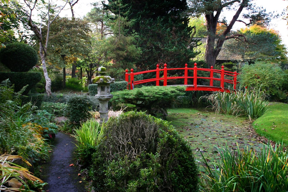 a red bridge over a small pond in a garden