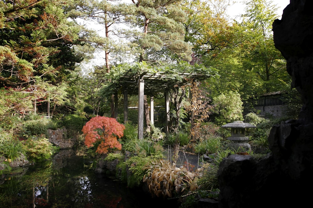 a garden with a pond and a gazebo surrounded by trees