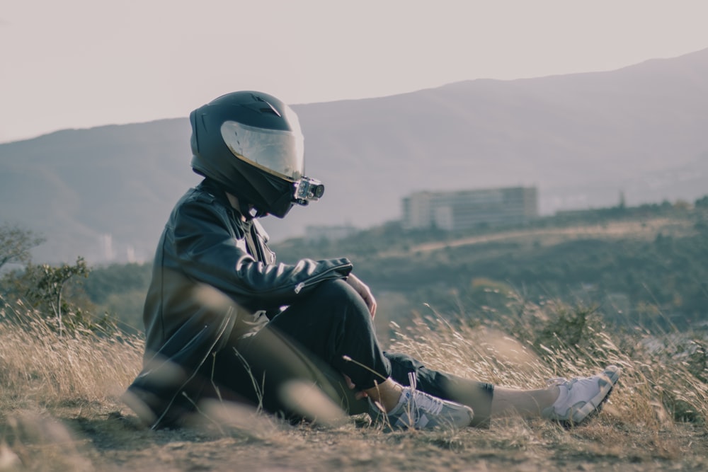 a person sitting in a field with a motorcycle helmet on