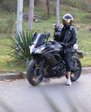 Rider wearing a neon-trimmed riding jacket stopping to check their bike on a country road.