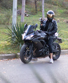 Rider wearing a neon-trimmed riding jacket stopping to check their bike on a country road.
