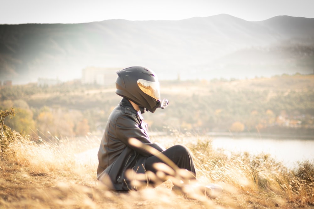 a person sitting in a field with a motorcycle helmet on