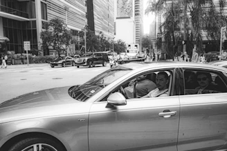 A black and white photo of a bustling Tirana street in the 1990s with vintage cars and pedestrians.