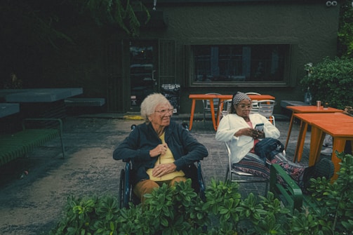 an elderly woman sitting in a wheel chair next to a man