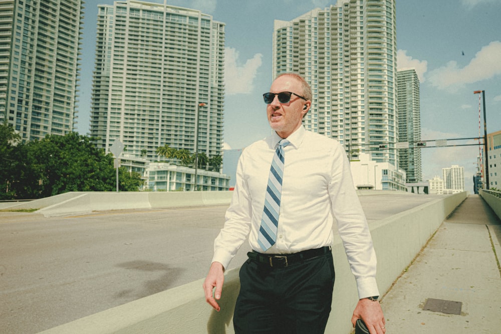 a man in a tie and sunglasses walking down a sidewalk