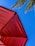 A red umbrella at an angle with a blue sky and palm tree leaves partially visible in the background.