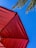 A red umbrella at an angle with a blue sky and palm tree leaves partially visible in the background.