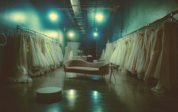 A cozy, stylish boutique interior with racks of elegant gowns and suits softly lit by warm lighting.