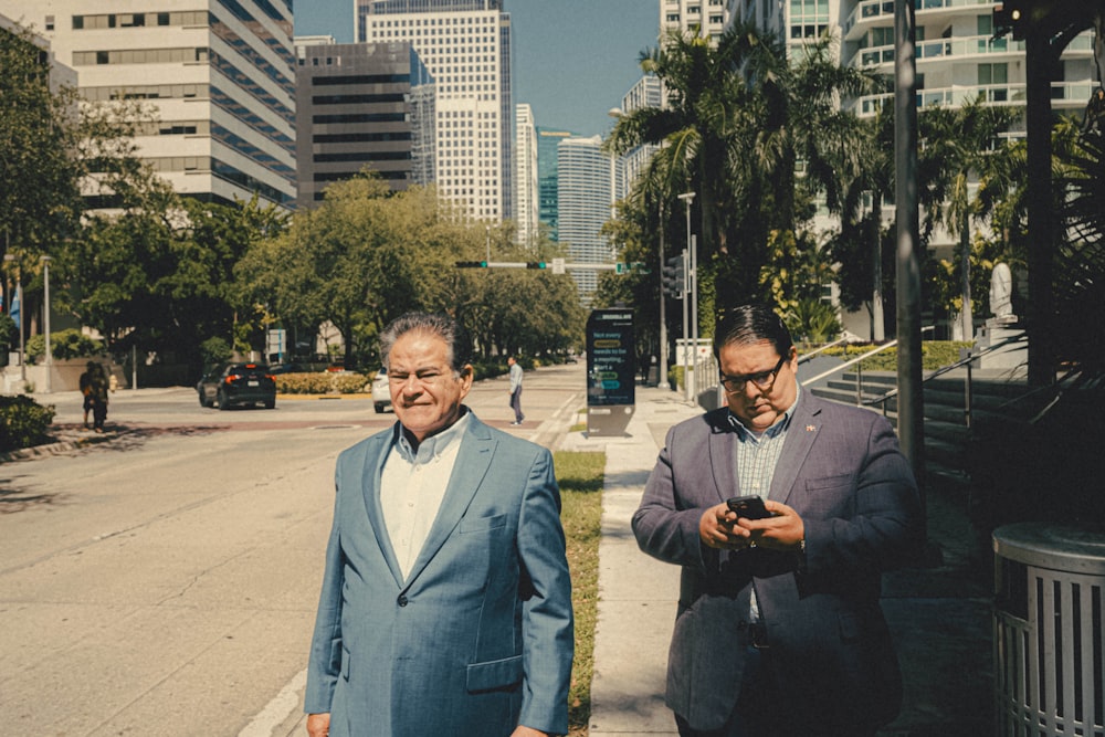 two men walking down a street while looking at their cell phones
