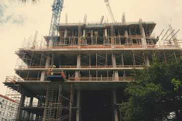 Modern commercial building framed by cranes and workers in safety gear, showcasing progress.