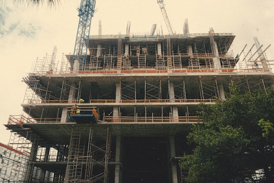 Construction workers collaborating on a building site with cranes and scaffolding in the background.