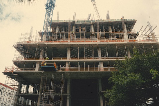 Construction workers collaborating on a building site with cranes and scaffolding in the background.