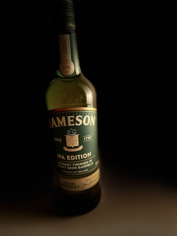 A Jameson whiskey bottle labeled as an IPA edition. The label indicates it's finished in craft beer barrels and originates from Ireland. The bottle is placed against a dark background, highlighting its green and black colors with gold accents.