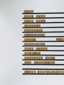 A menu board with various coffee and tea options like drip, pour over, cold brew, and more. Each item is displayed using wooden block letters lined up horizontally.