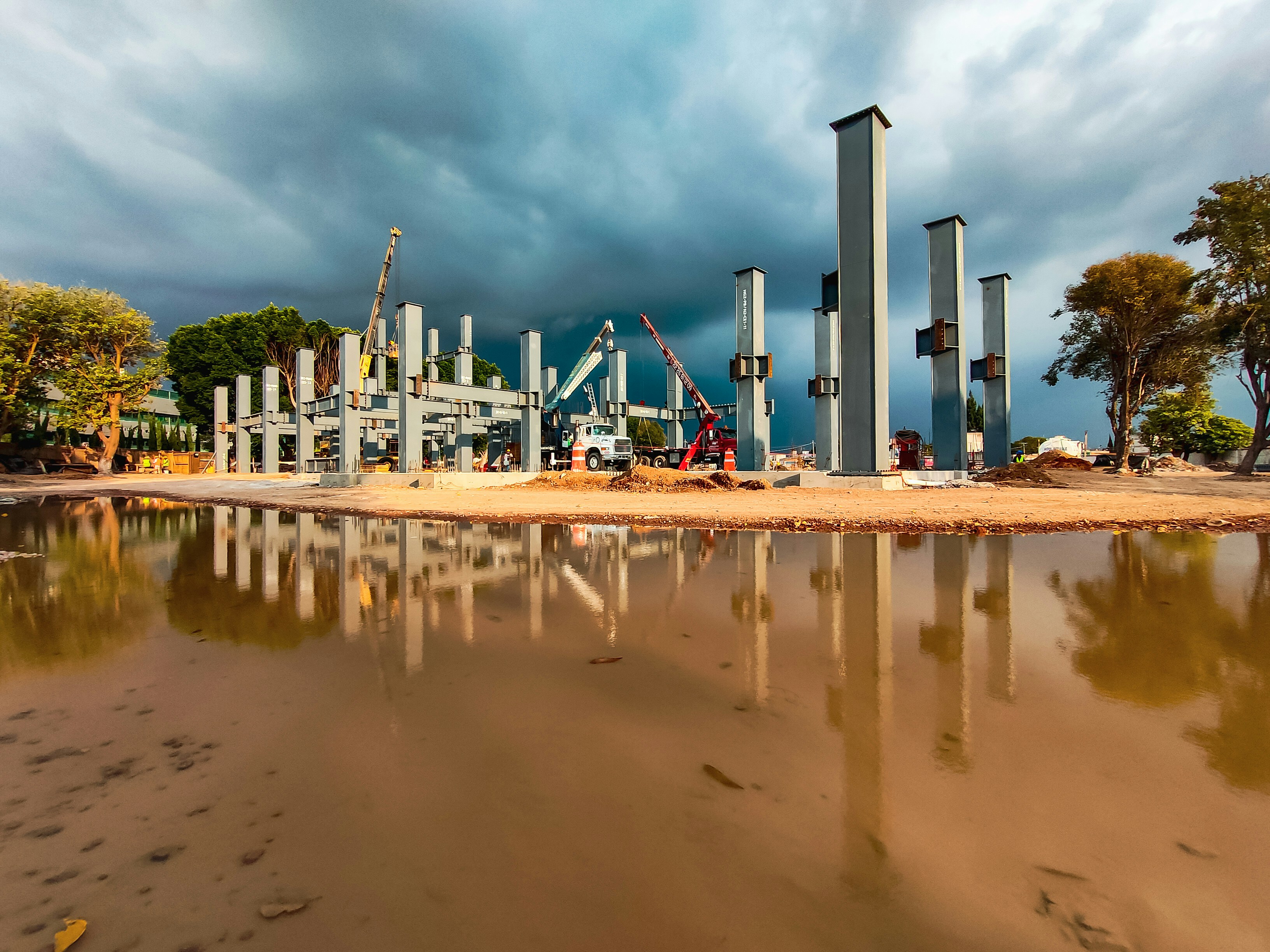Modern commercial building under construction with steel framework and cranes, dramatic sky, professional construction site