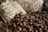 A pile of chestnuts is spread out, with some displayed in front of burlap sacks that have text printed on them. The background includes clear plastic bags filled with walnuts or similar nuts, suggesting a market or farm setting.