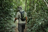Man wearing a dark olive t-boy tactical backpack hiking through dense forest.