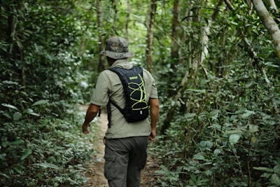 Man wearing a dark olive t-boy tactical backpack hiking through dense forest.