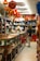 A store aisle filled with various items, including red hanging lanterns, shelves stocked with ceramics, souvenirs, and decorative objects. Several people are browsing the merchandise. The store is brightly lit with a warm ambiance.
