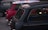 A group of classic Mini Cooper cars parked closely together. The car in the foreground is black with a partial soft top open and has the words 'British Open' inscribed on it. The car behind it is red with a roof featuring the design of the Union Jack. A green Mini Cooper is also visible, parked alongside.