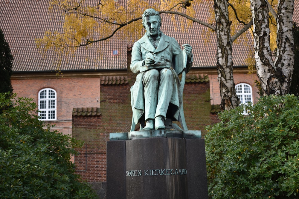 une statue d’un homme assis sur un piédestal devant un bâtiment