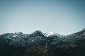 A serene mountain range under a soft blue sky with gentle white clouds.