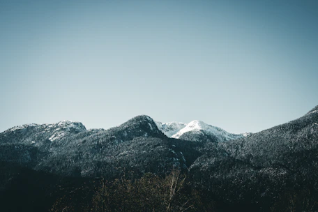 A serene mountain range under a soft blue sky with gentle white clouds.