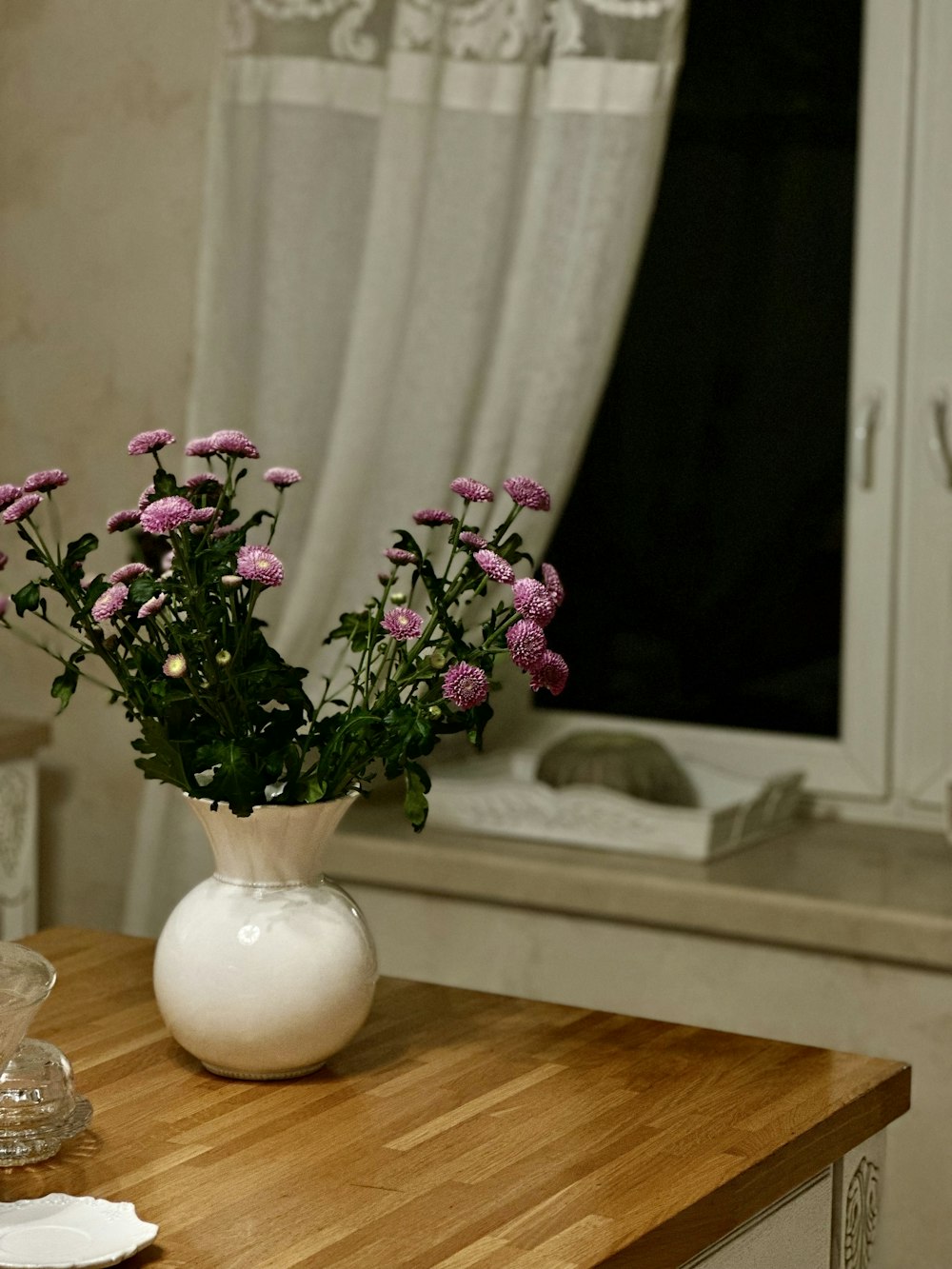 a white vase filled with purple flowers on top of a wooden table