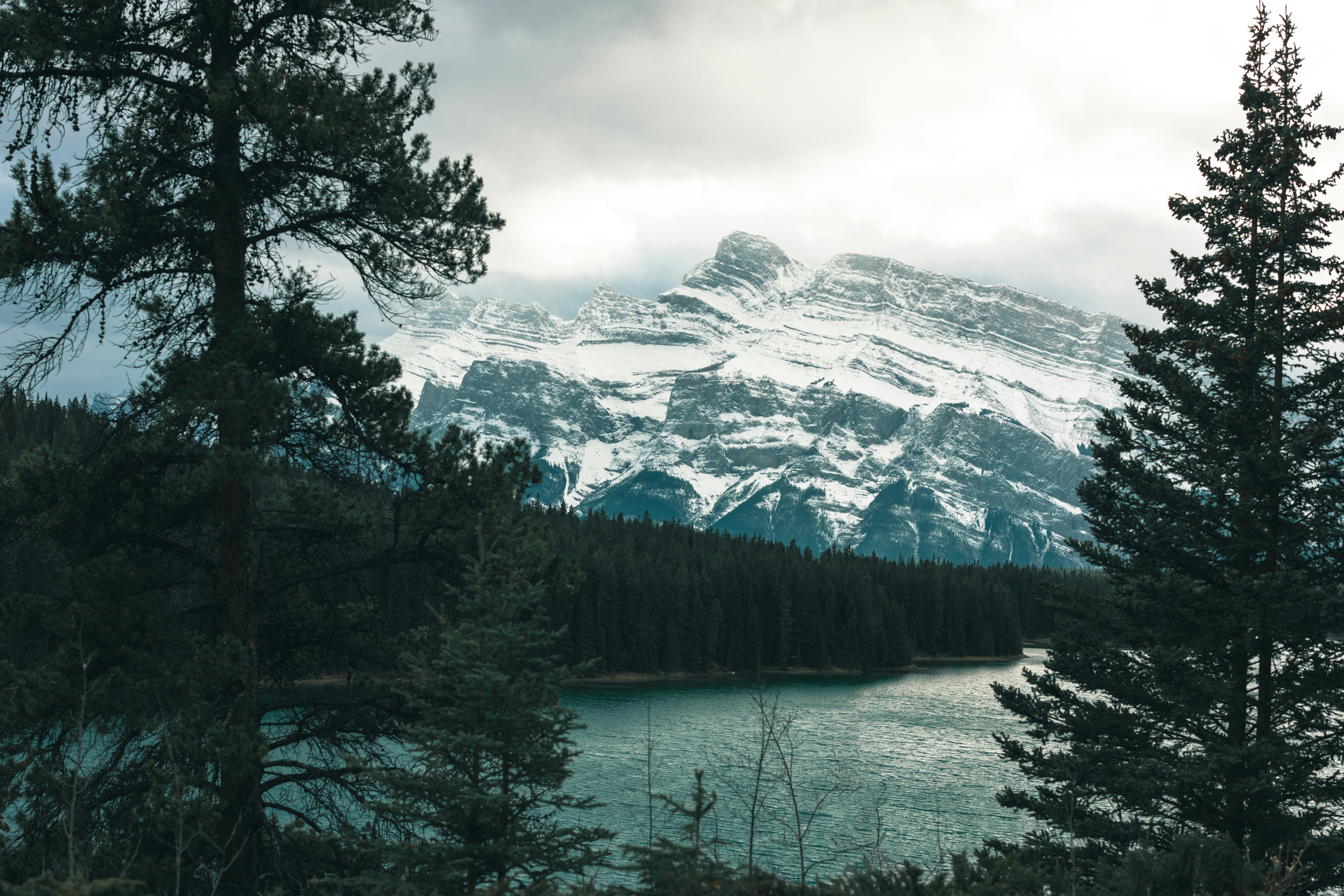 a snow covered mountain with a lake in the foreground, The road through the great Canadian rockies