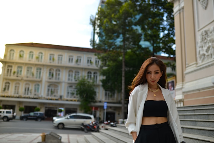 A chic woman wearing a tailored blazer and sleek trousers, standing confidently in a sunlit urban setting.
