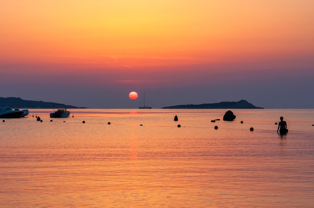 a sunset over a body of water with boats in the distance