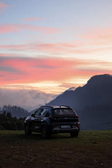 A comfortable car parked by a scenic mountain road near Mussoorie at sunset.