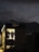 A small, illuminated shop or cabin displays hanging clothes, including jackets and shirts. The shop is situated in a dark, outdoor setting with a mountainous landscape in the background. The sky is dusky, with a visible crescent moon and scattered clouds, creating a serene ambiance.