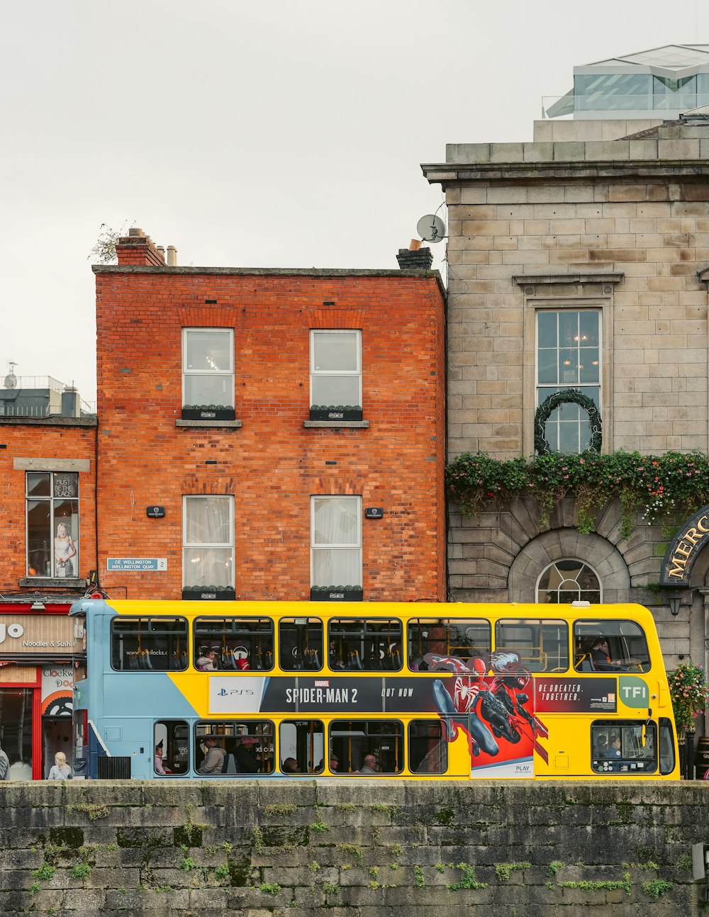a yellow and blue double decker bus parked in front of a brick building
