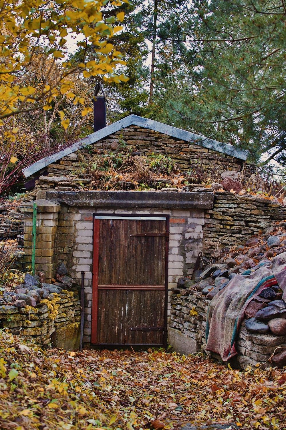 a small building with a wooden door and a pile of leaves on the ground