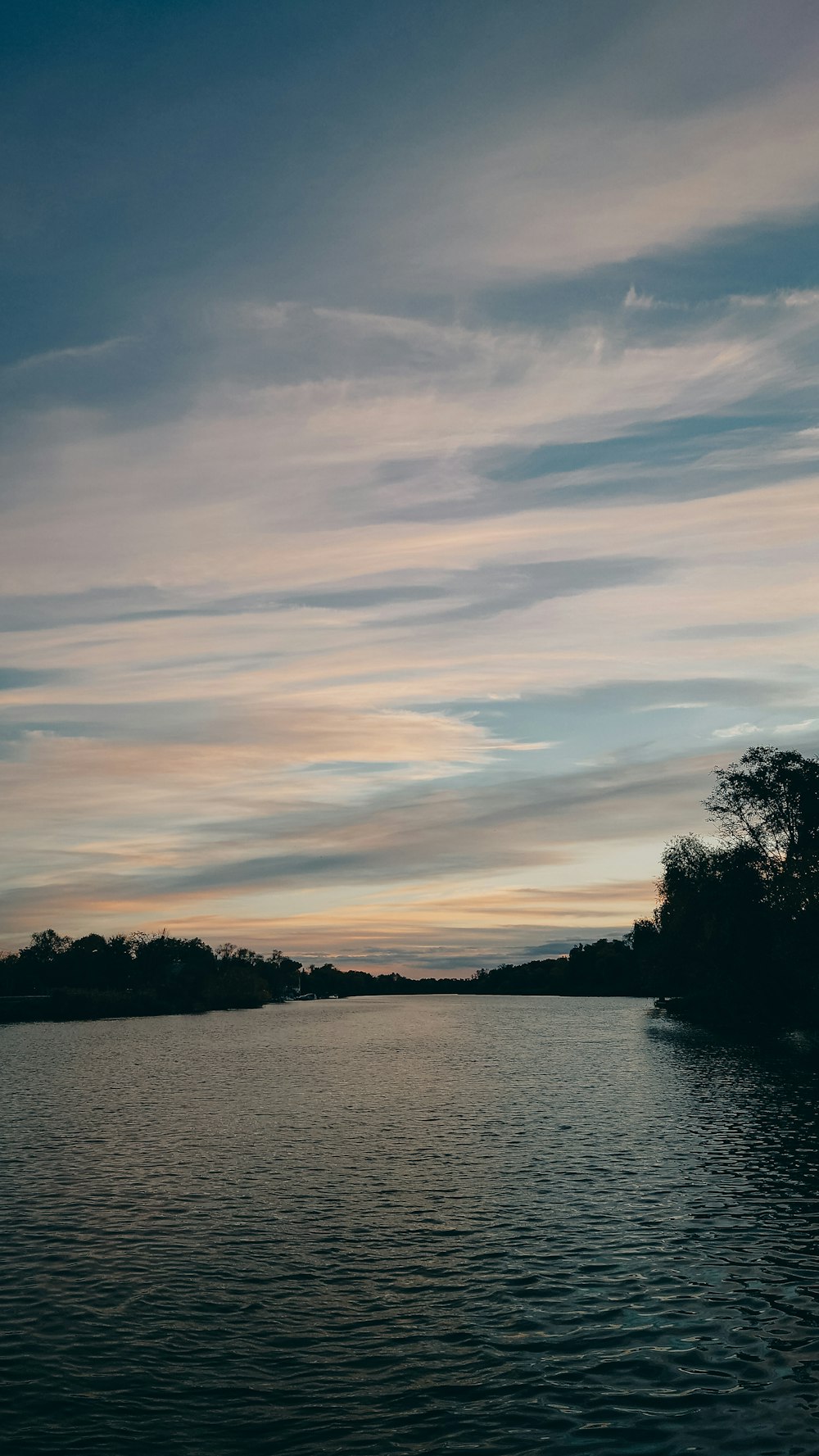 a body of water surrounded by trees under a cloudy sky