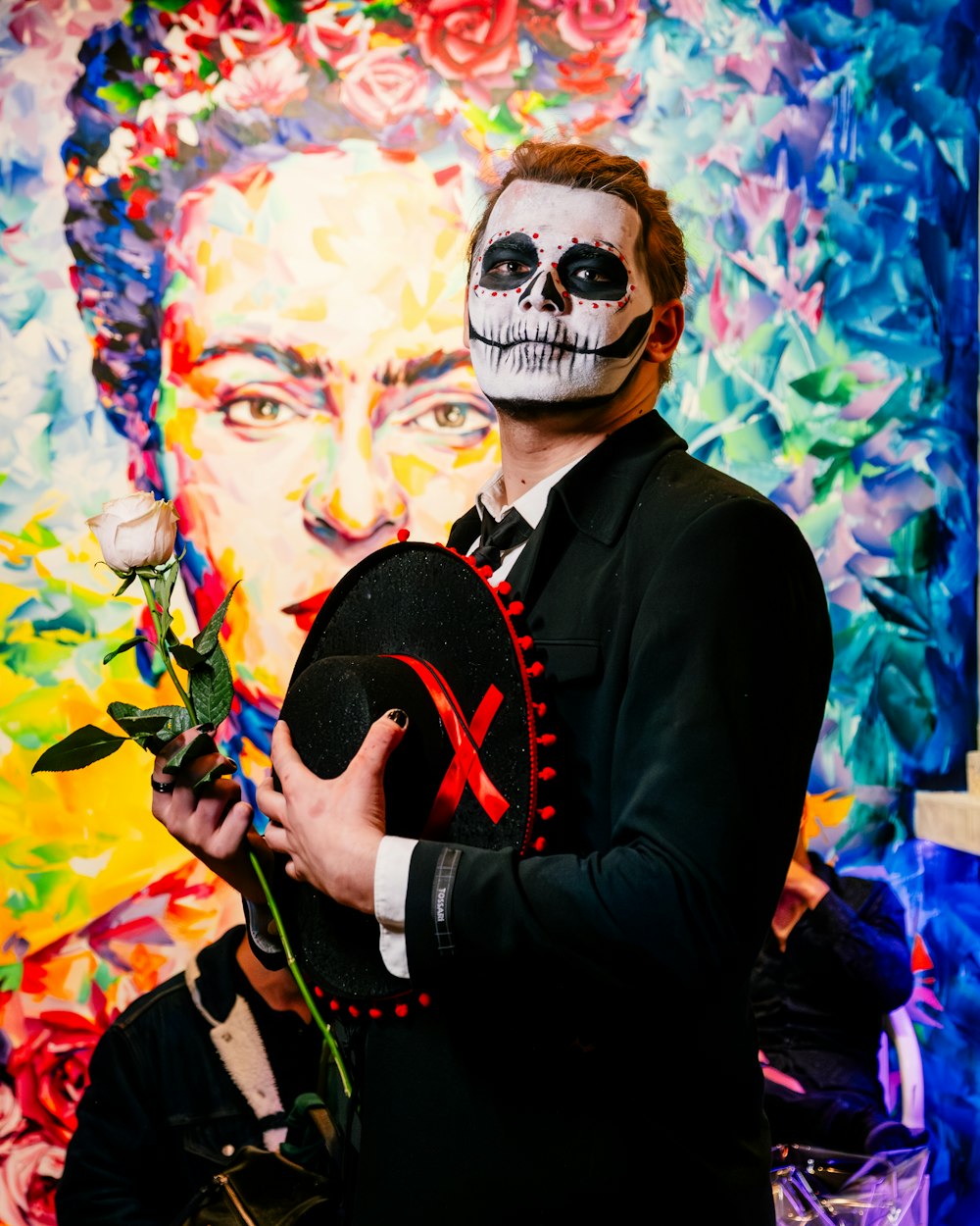 a man in a suit and skull makeup holding a flower