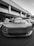 A high-performance sports car is parked in front of a modern office building with large windows and columns. The car has a sleek design with a prominent front grille and aerodynamic features.