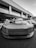 A high-performance sports car is parked in front of a modern office building with large windows and columns. The car has a sleek design with a prominent front grille and aerodynamic features.