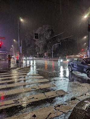 Street scene in rainy weather with reflections on wet pavement and lone figure holding umbrella.