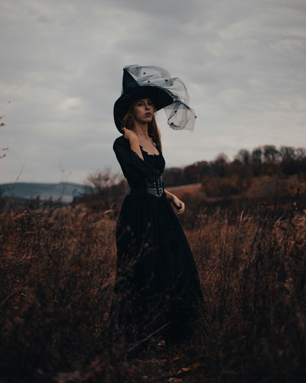 uma mulher com um vestido preto e chapéu em pé em um campo