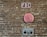 A brick wall features fire department connections including a red 'FDC' sign at the top, a circular pink 'Sprinkler Alarm' cover in the middle, and a metal auto sprinkler connection with two openings at the bottom.