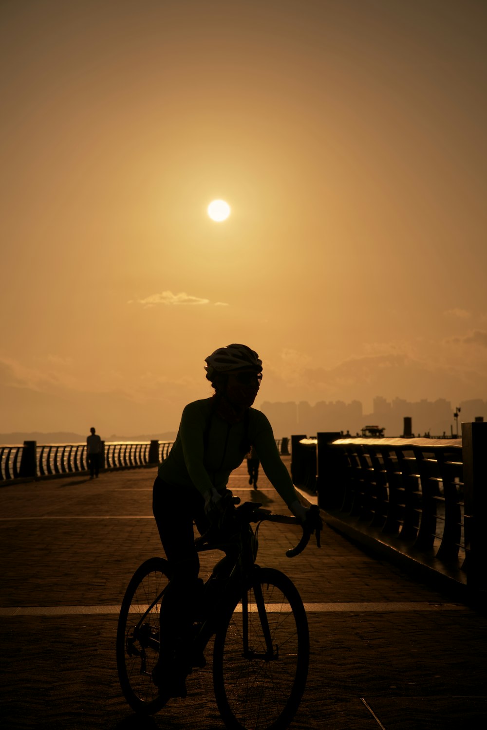 a man riding a bike across a bridge at sunset