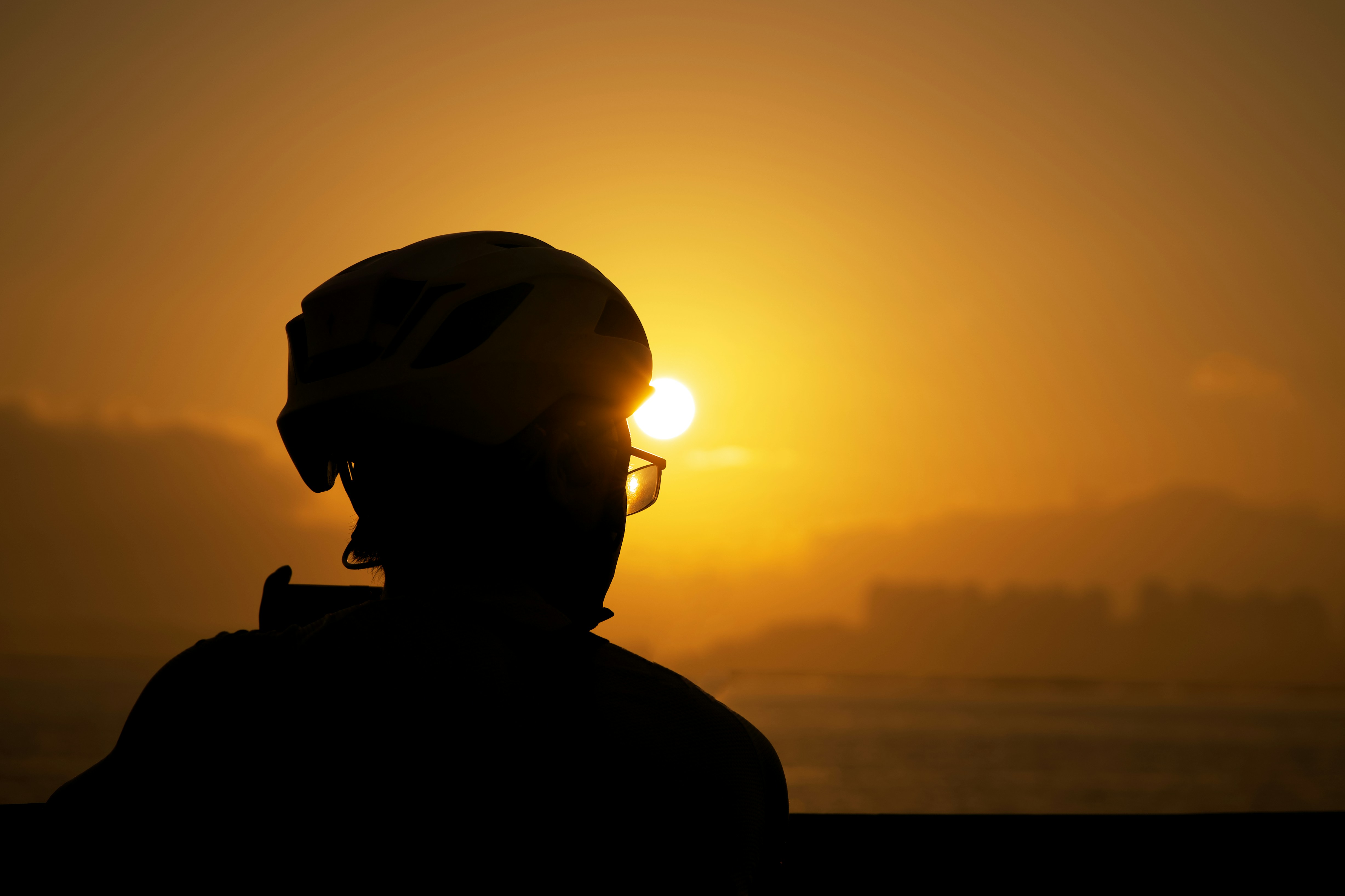 die Silhouette einer Person, die einen Helm trägt, mit der Sonne im Hintergrund