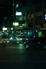 Nighttime urban street scene featuring sleek cars under neon red and blue lighting.