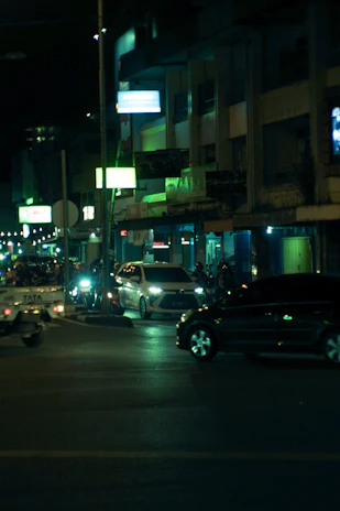 Nighttime urban street scene featuring sleek cars under neon red and blue lighting.