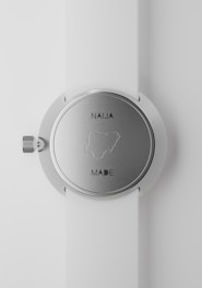 A close-up view of a silver wristwatch with a white strap. The back of the watch shows the outline of Nigeria, with the text 'NAIJA MADE'. The watch's crown is visible on the left side of the image.