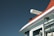 A close-up of a boat's cabin features a clean, modern design with a large pipe or exhaust on the rooftop and stainless steel railing. The cabin is mostly white with a striking red accent at the top, set against a clear blue sky.