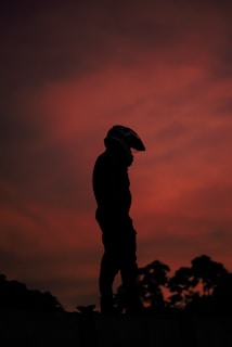 A rider silhouetted against the rising sun, helmet reflecting the fiery orange light.