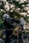 A person wearing a helmet and protective gear sits on a Royal Enfield motorcycle. The motorcycle is parked outdoors with a blurred background of trees. The scene is focused on the rider and the detailing of the motorcycle, including its rugged design and frontal headlight.